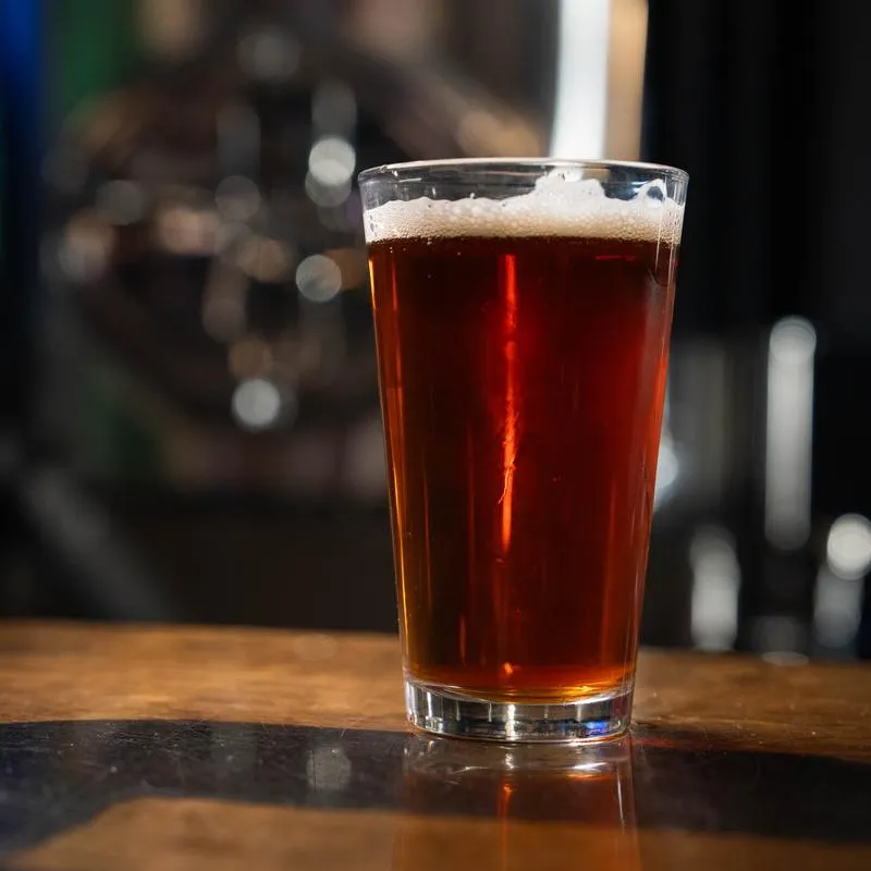 Amber beer in a pint glass with foam on a bar counter.