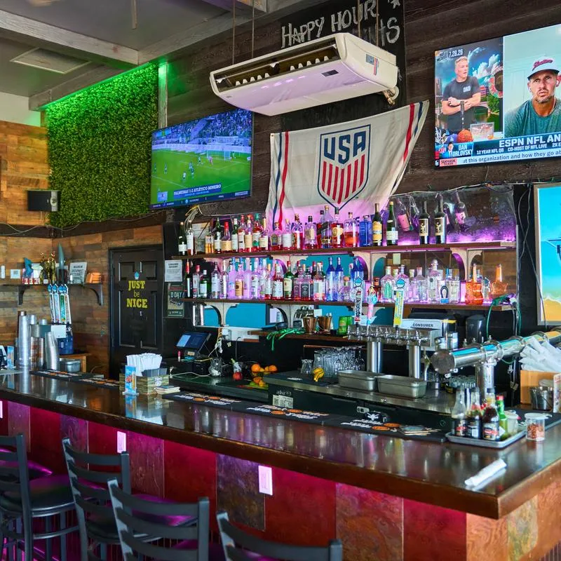 Bar featuring a wooden bar counter with red under-glow lighting, bar stools and liquor shelves.