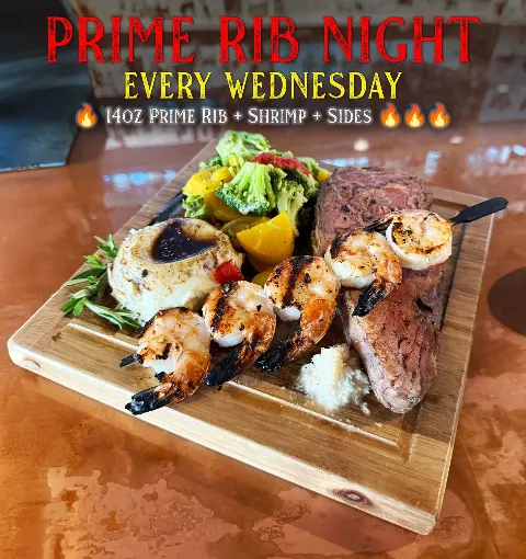 A wooden serving board with a prime rib dinner that includes grilled shrimp, mashed potatoes with gravy, mixed vegetables, and a slice of prime rib. The image promotes Prime Rib Night every Wednesday,