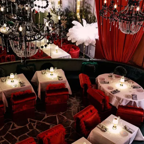 Interior with tables and chairs, red velvet curtains and elaborate chandeliers.