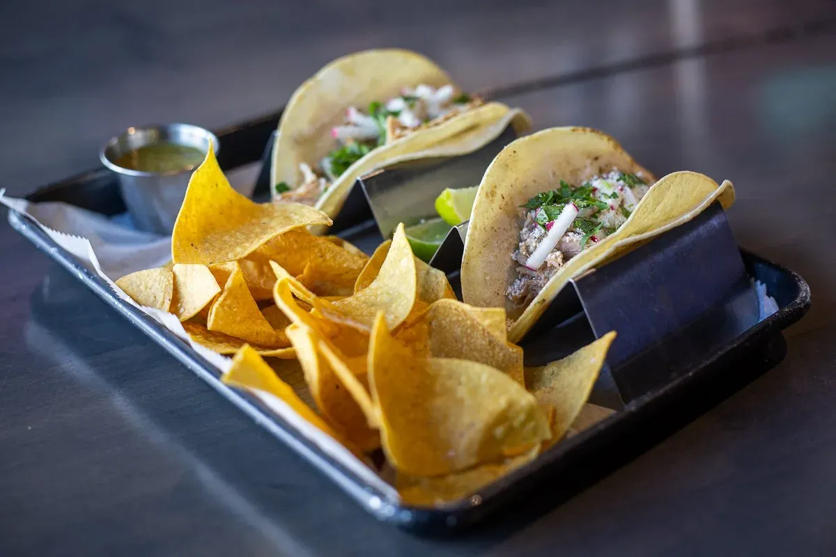 A tray of tacos and tortilla chips on a table.