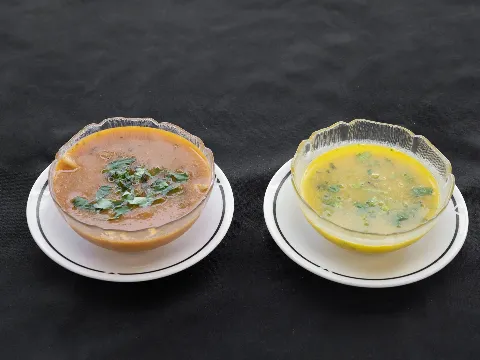 Two bowls of soup on white plates, one brown with green garnish, one yellow with green herbs.