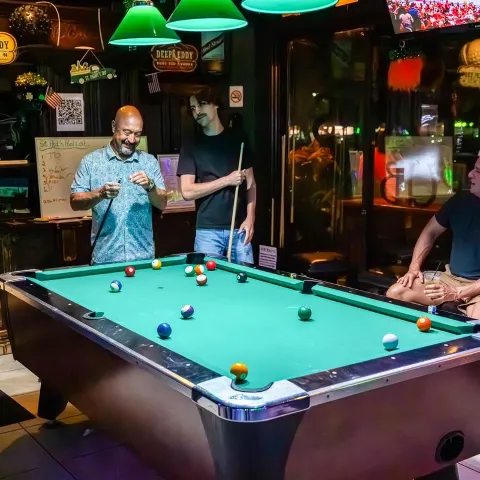 People playing on a pool table in a dimly lit bar setting.