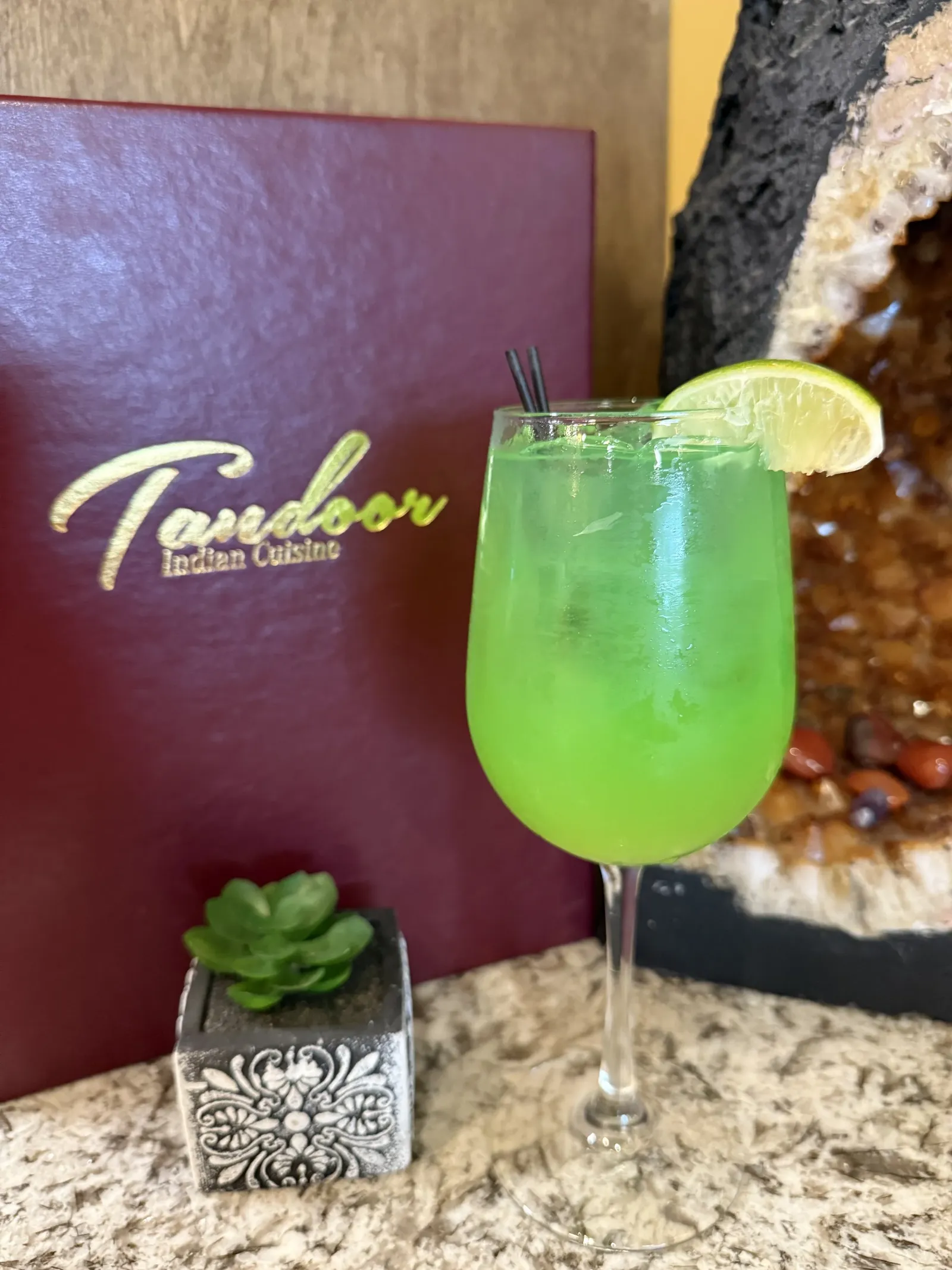 Green cocktail with lemon wedge garnishment on a restaurant bar counter.
