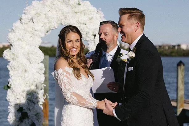 bride and groom standing with their officiant under an arbor of white flowers at their waterfront ceremony on Lemon Bay in Englewood, FL