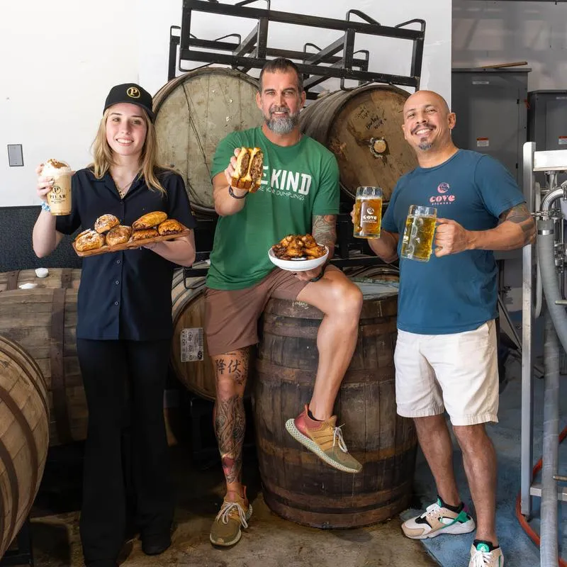 Three people in a brewery posing with food and drinks.