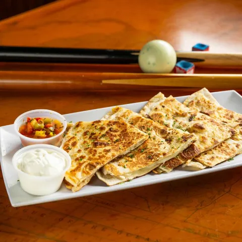 Cheese quesadillas on a table with pool cues, chalk, and a ball.