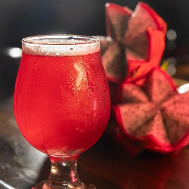 Pink dragon fruit beer in a tulip glass with sliced dragon fruit on a counter.