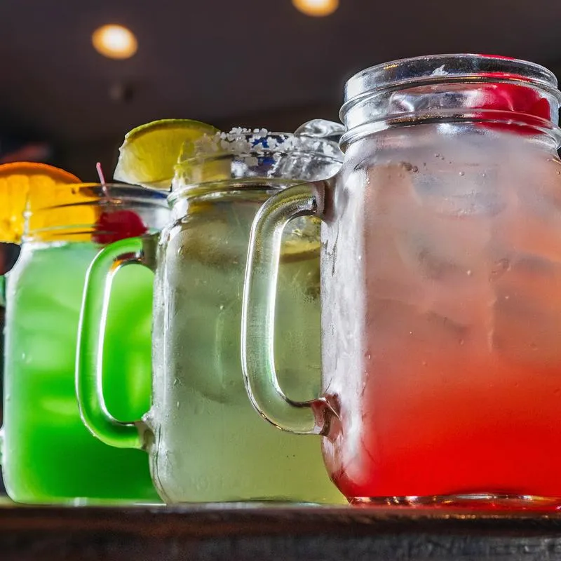 Colorful drinks with fruit garnishes in mason jars.