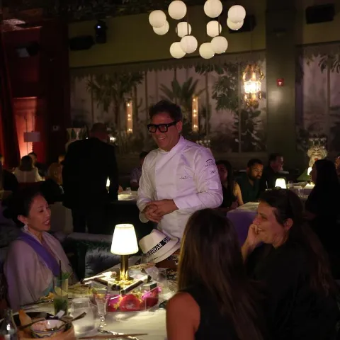 Chef speaking with guests at lamplit dining table.