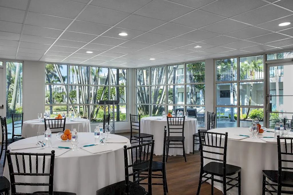 Bright room with tables set for dining, large windows, and palm trees outside.