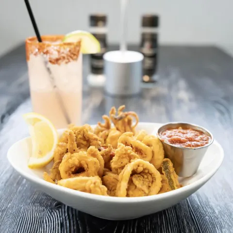 Fried calamari served with dipping sauce and lemon, accompanied by a cocktail.