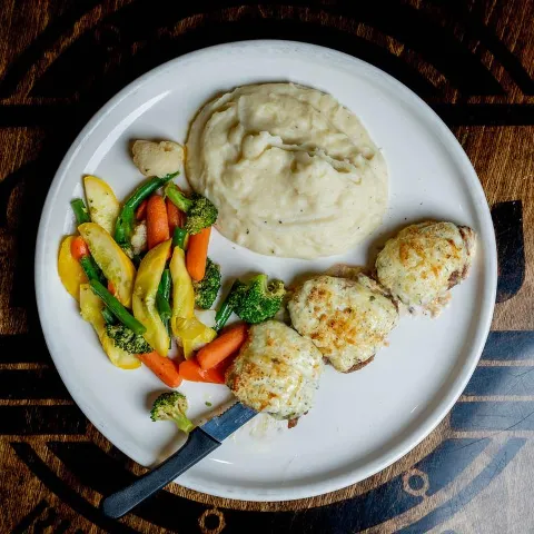 Chicken topped with melted cheese accompanied by mashed potatoes and mixed vegetables.