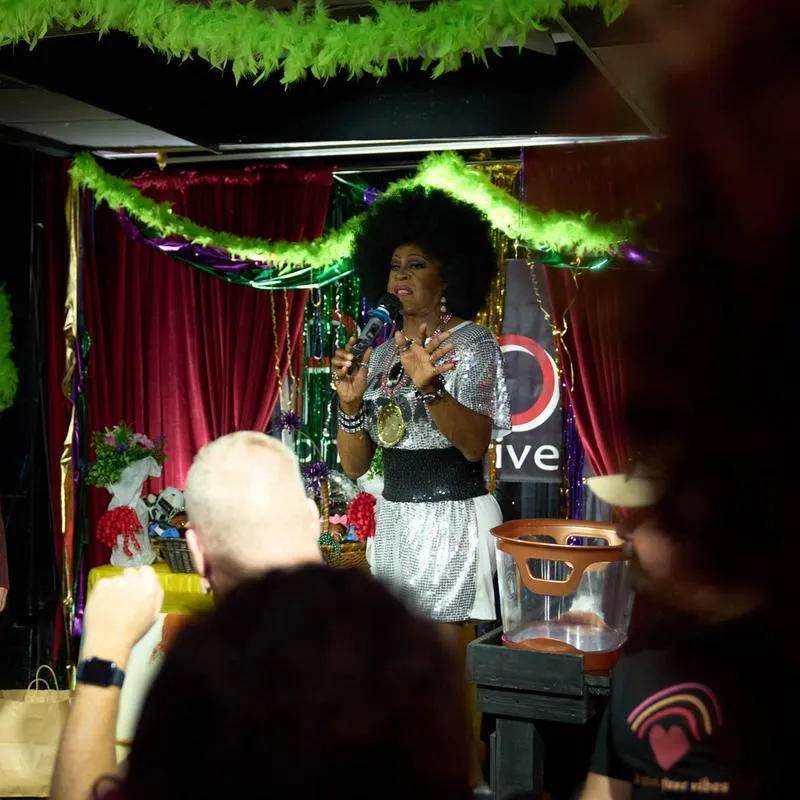 Performer speaking into a microphone on a decorated stage in front of an audience.