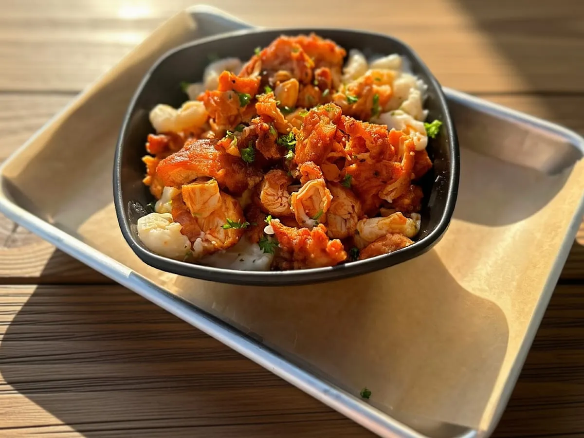 Buffalo Chicken Mac N' Cheese, cavatappi topped with crispy buffalo chicken and parsley, in a black bowl on a paper-lined tray