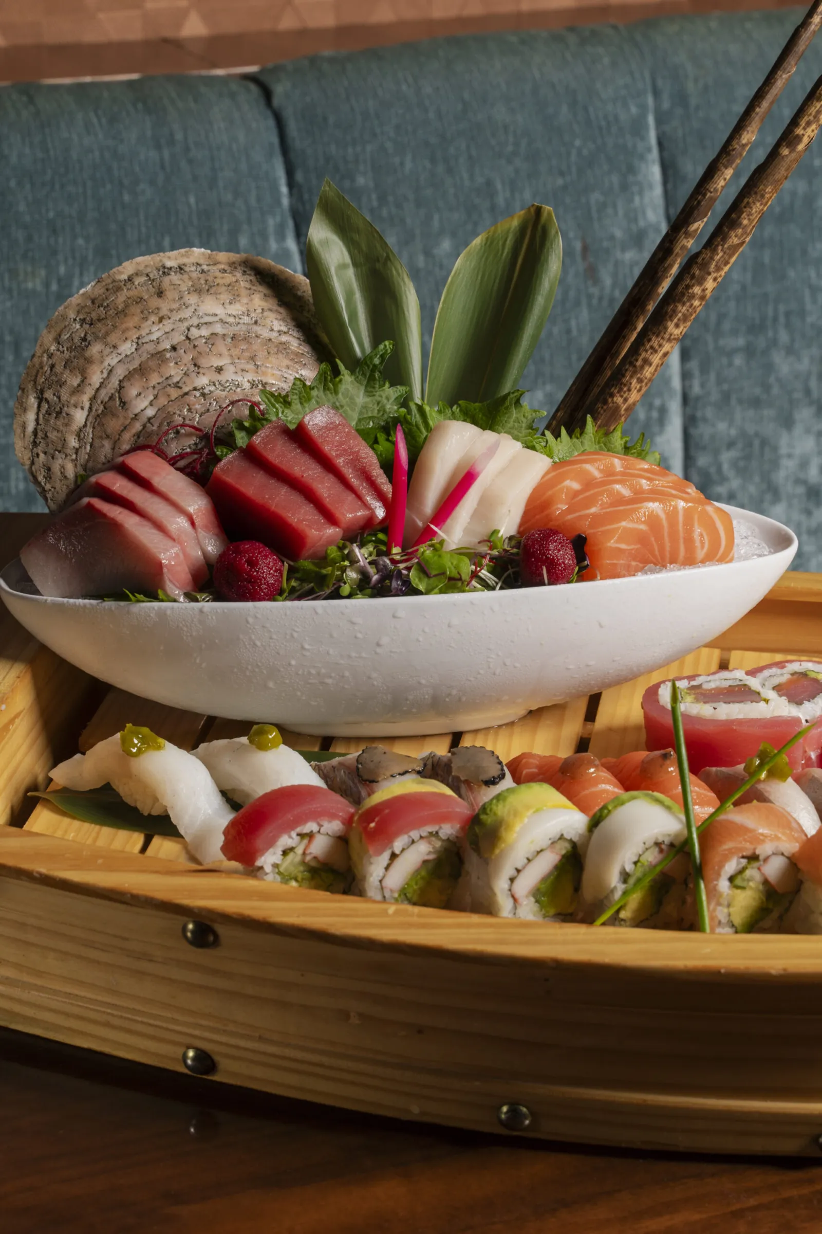 Sushi boat presentation featuring a bowl of assorted fresh sashimi and a wide variety of sushi rolls and nigiri on the wooden deck