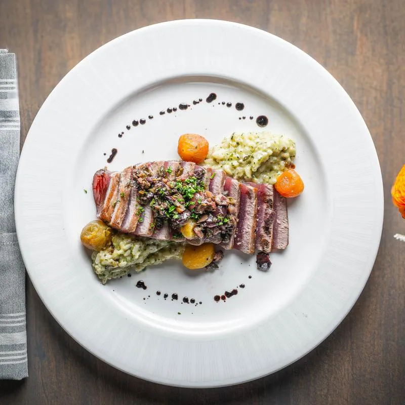 Seared ahi tuna with tomatoes on a white plate.