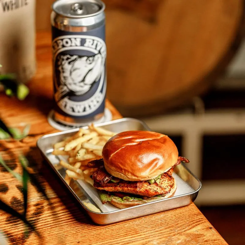 Crispy chicken sandwich with bacon, lettuce, pickles, fries, and a craft beer can.