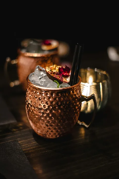 Copper mug with a drink, ice, garnish, and black straws on a dark table