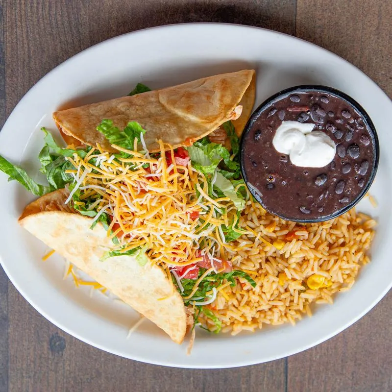 Tacos, served with lettuce, tomato, cheese, rice, and refried beans.