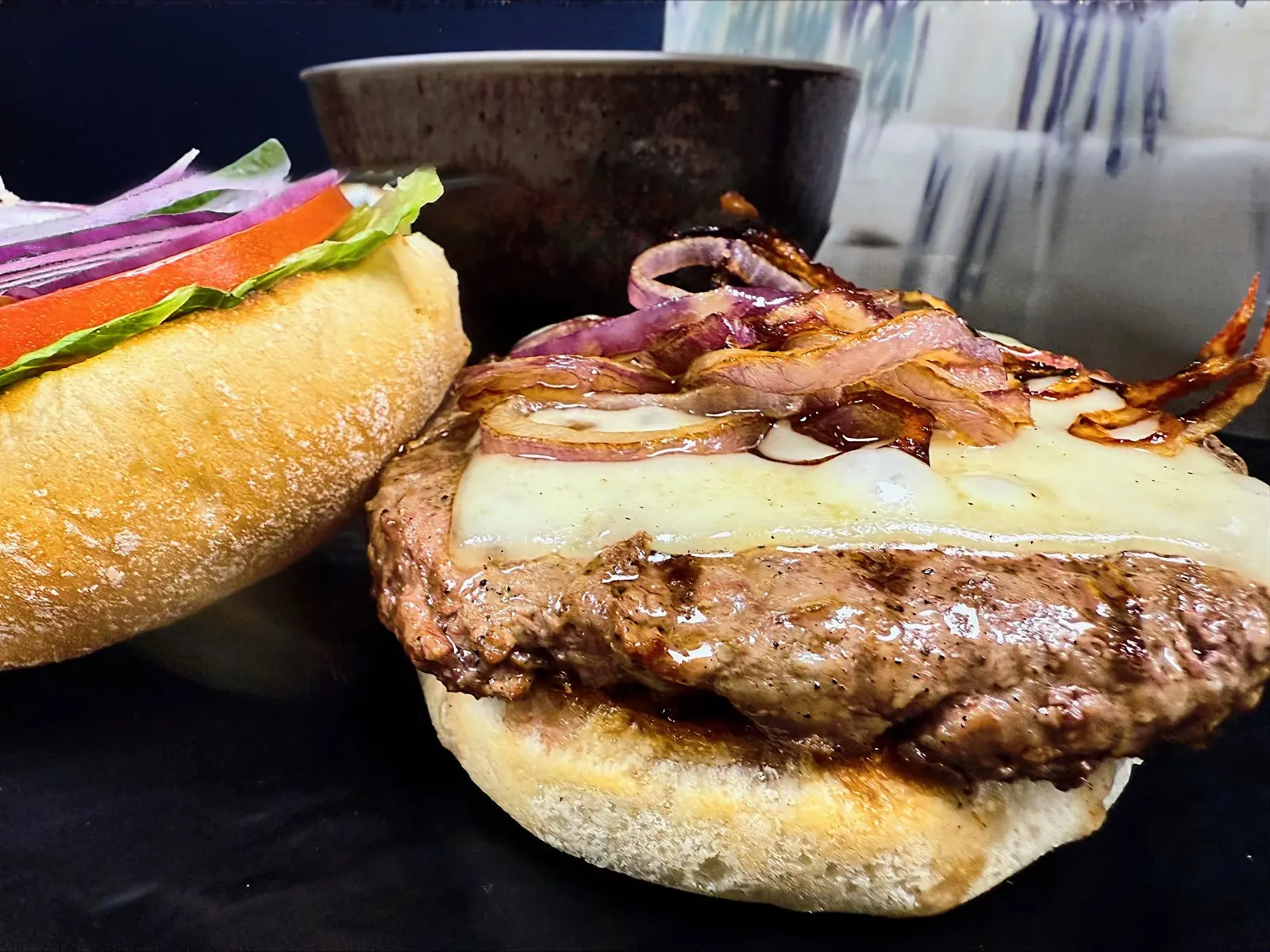 Close-up of a gourmet cheeseburger with grilled onions, lettuce, tomato, cheese, and red onion on a bun, prepared for serving.