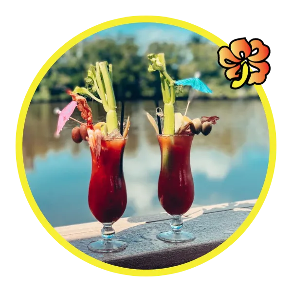 Two glasses of drink with a flower and water in the background.