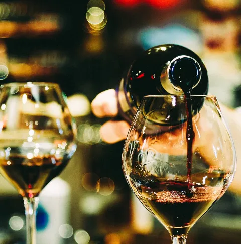 A glass of red wine being poured from a bottle, with another glass nearby.