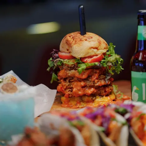 Tucker Duke Burger served alongside other meals, bottle of beer and a cocktail.