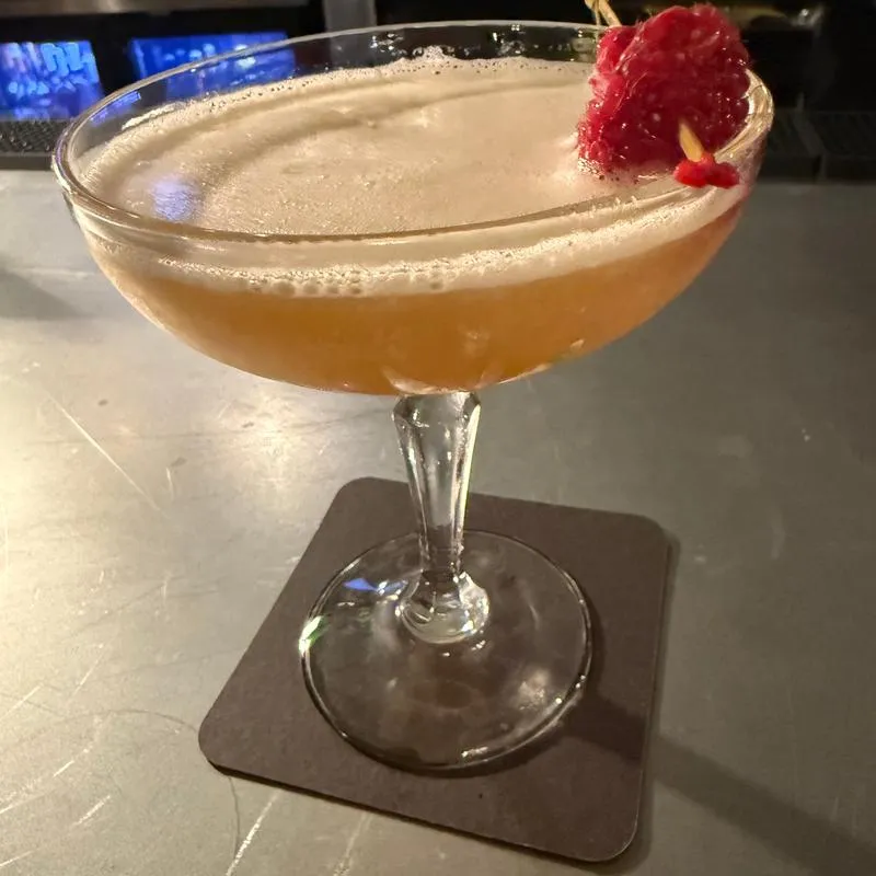 Cocktail served in a coupe, garnished with a single raspberry.