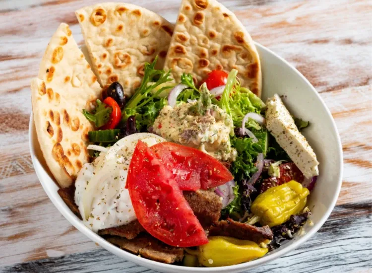 Delicious Greek Salads at Acropolis Taverna, showcasing the Acropolis Salad that comprises of Tomato, cucumber, onion, pepperoncini, kalamata olives, and lettuce mix. Topped with gyro, potato salad, p