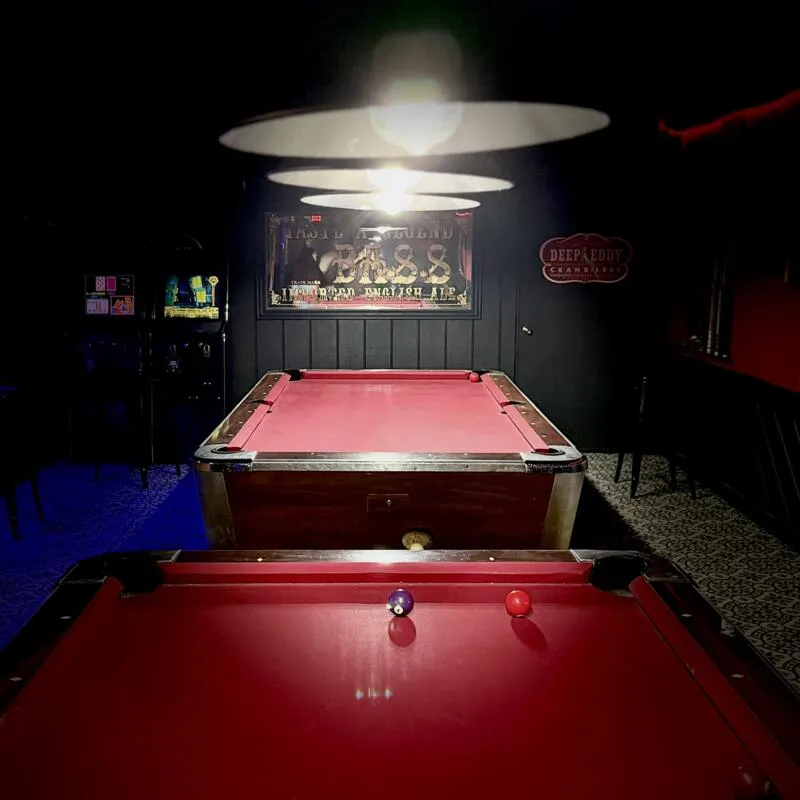 Pool tables under lights in a dim lit game room.