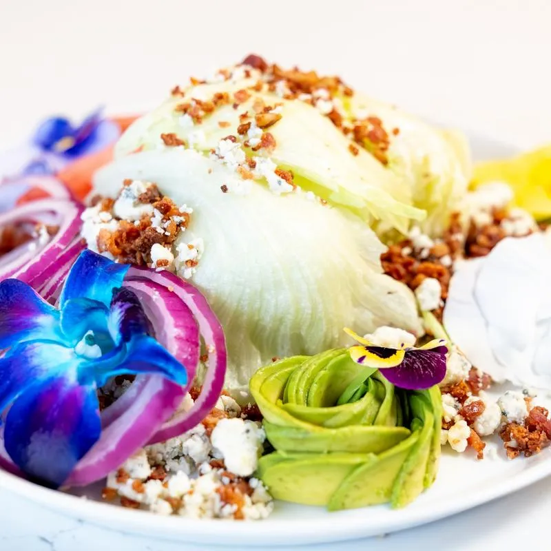 Wedge salad with bacon, avocado, gorgonzola, and orchid garnish.