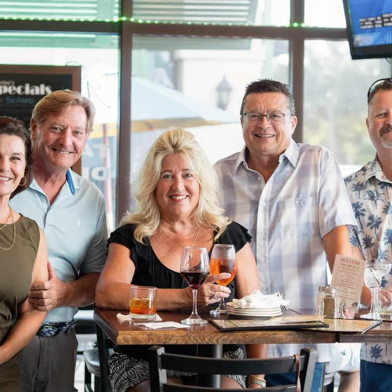 Owners, guests, and people at the bar are posing for a photo..