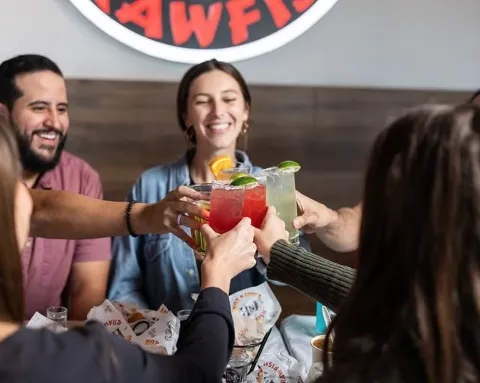 People celebrating with colorful cocktails at a restaurant or bar, raising their drinks in a toast.