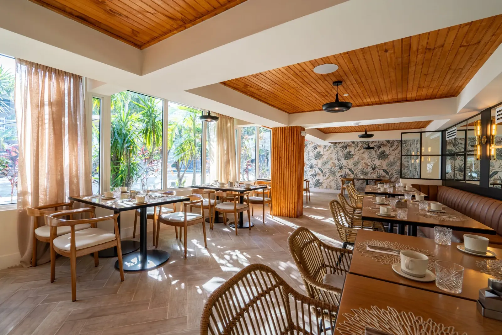 Sunlit dining room with wooden tables, woven chairs, and garden views