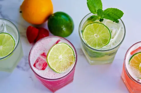 Three different colored drinks with lime slices and strawberries on a table.
