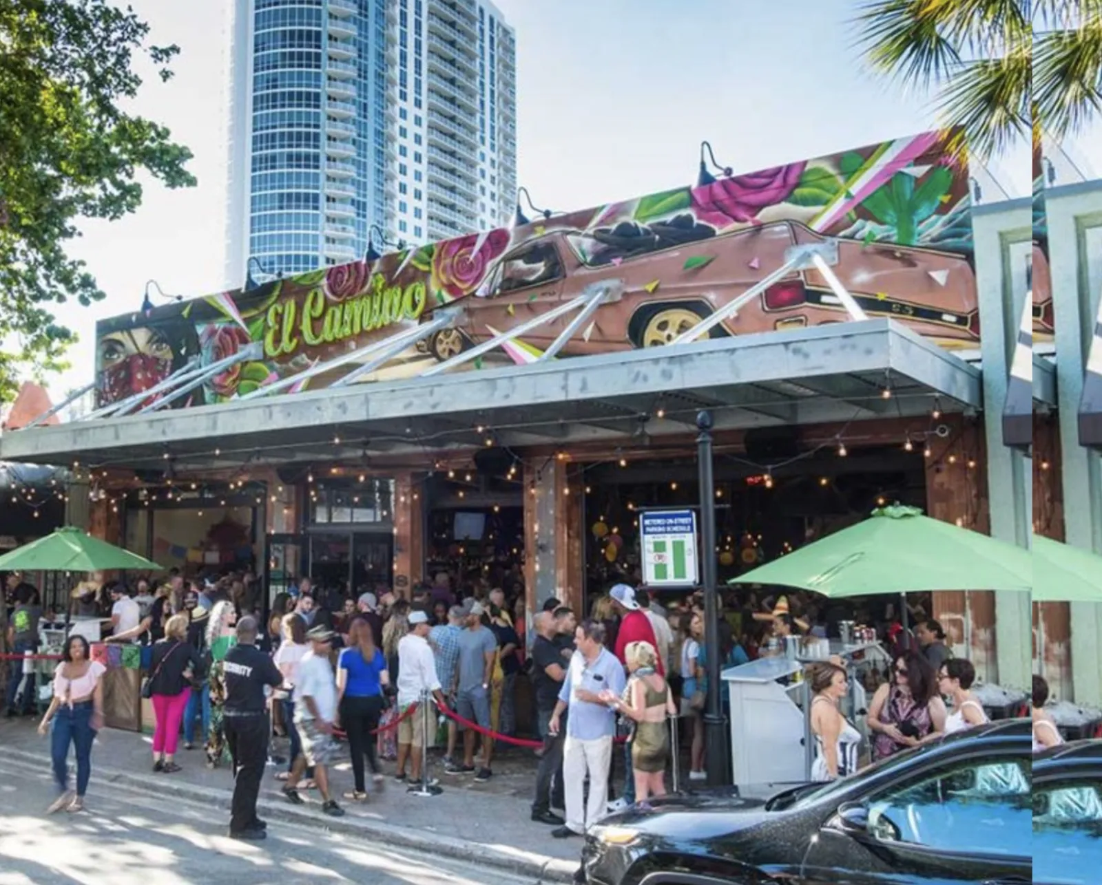 El Camino Fort Lauderdale storefront at dusk with mural of a vintage car and roses, illuminated sign, string lights, and crowd of patrons gathered outside
