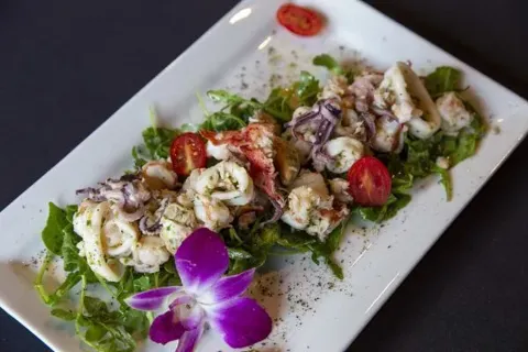 Seafood salad with tomatoes and an orchid flower on a white plate.