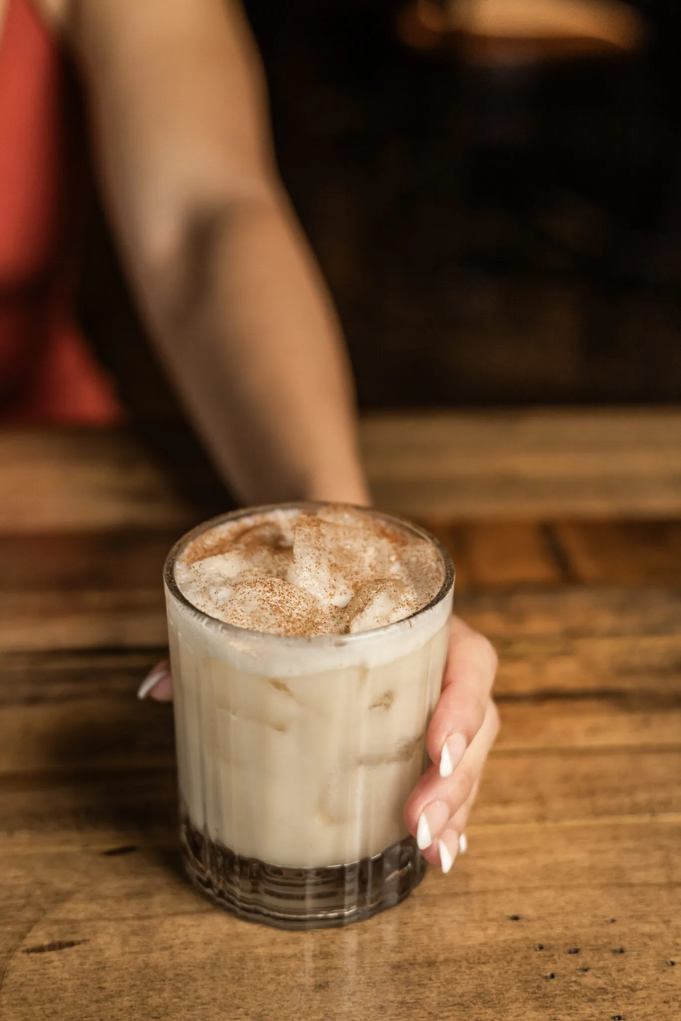 Hand holding iced cinnamon latte on wooden table
