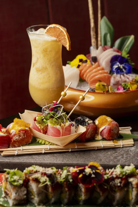 Variety of specialty sushi rolls garnished with fish roe and edible flowers, served with a frozen tropical cocktail.