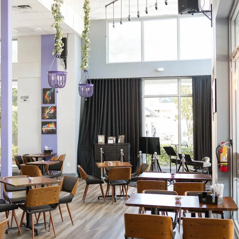 Interior with tables, chairs, hanging lights, dark accent curtains and light wood flooring.