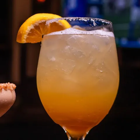 Cocktail on the rocks, with and orange wedge.