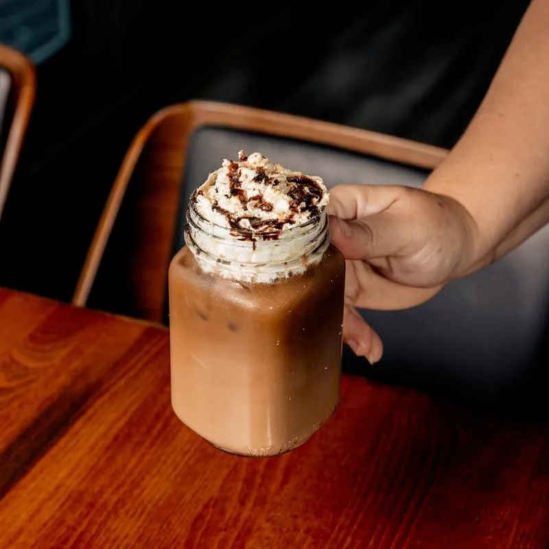 Hand holding a jar with iced coffee above the table.