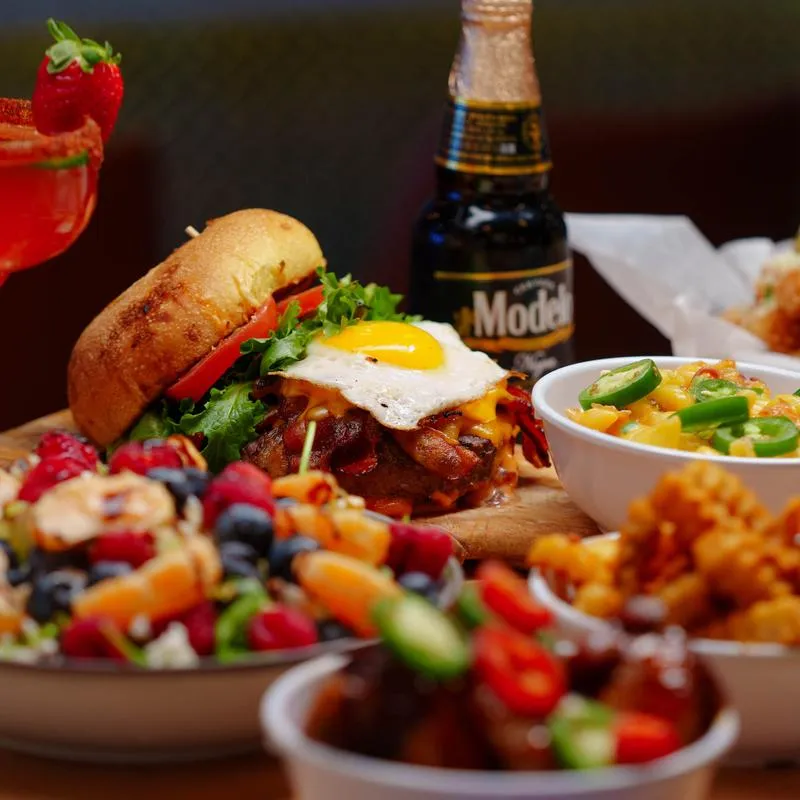 Assortment of dishes served on the table with a cocktail and a bottle of beer.