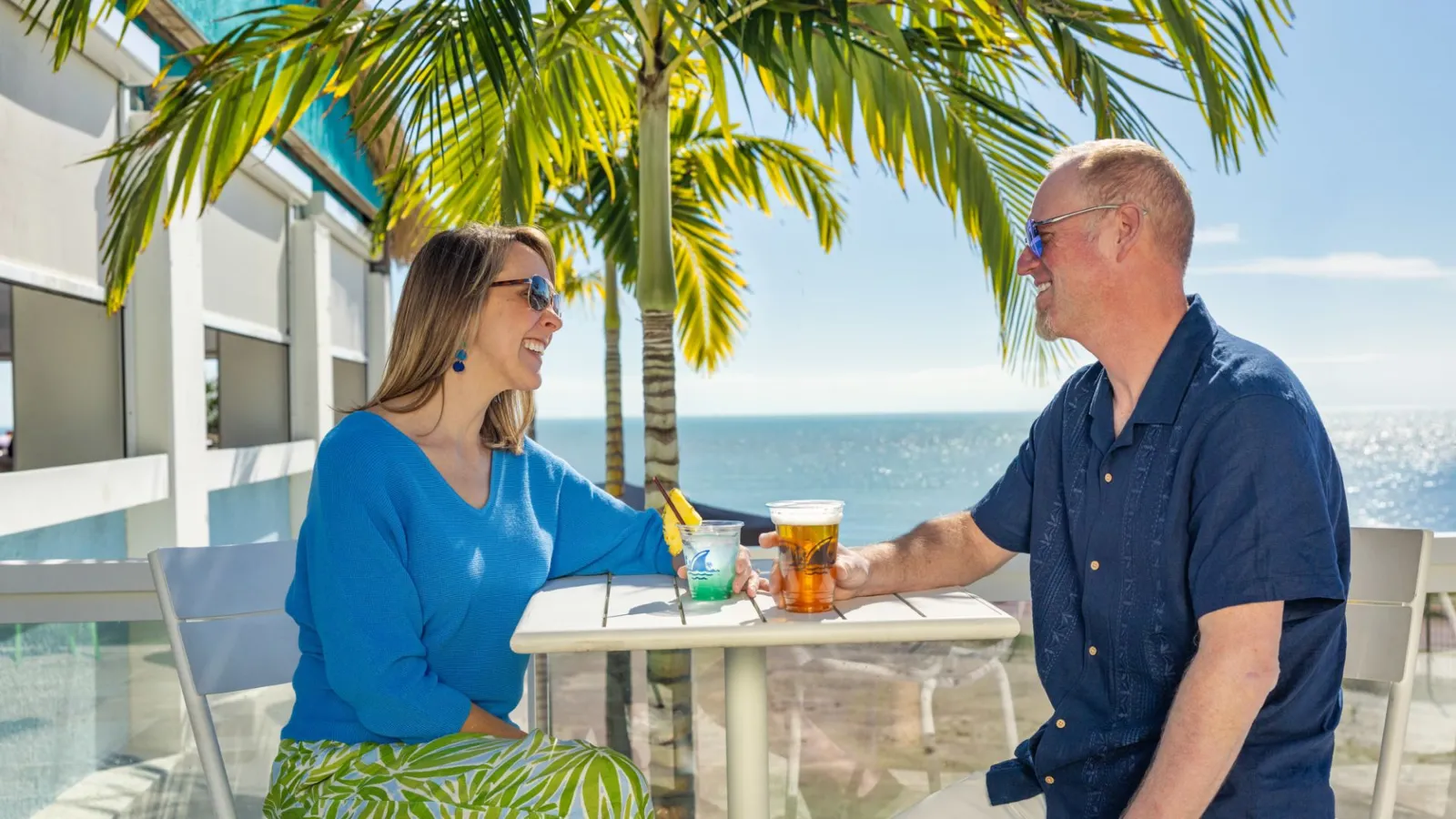 A Man And Woman Sitting At A Table With Drinks On It