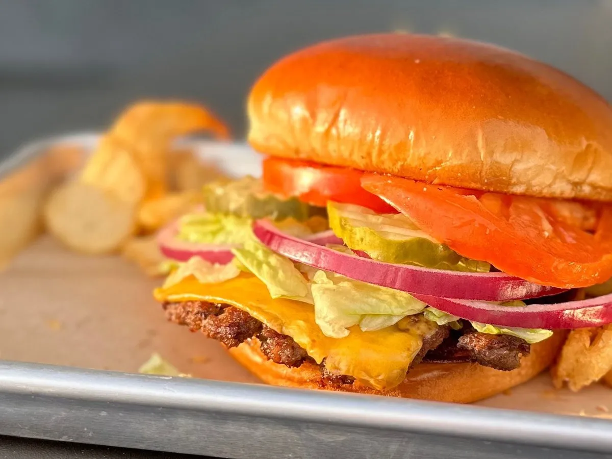 A Classic American Smash Burger with cheese, lettuce, tomato, onion and pickles, fries on the side