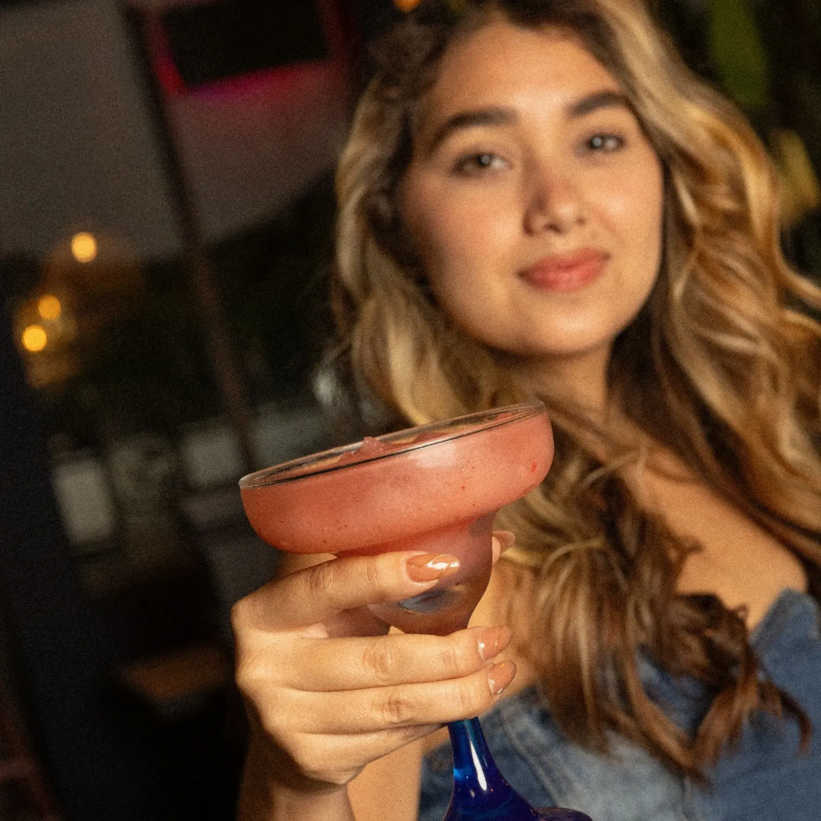 Woman holding a pink margarita, smiling.