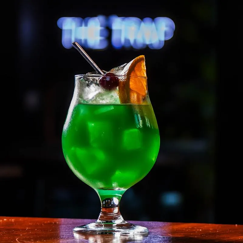 A green craft cocktail with orange and cherry garnish