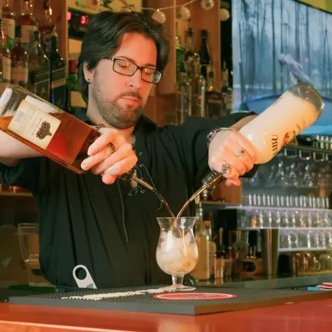 Bartender free pouring from two bottlws into a glass.