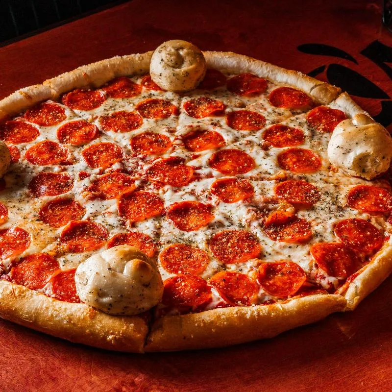 Pepperoni pizza and several baked garlic knots placed along the crust.